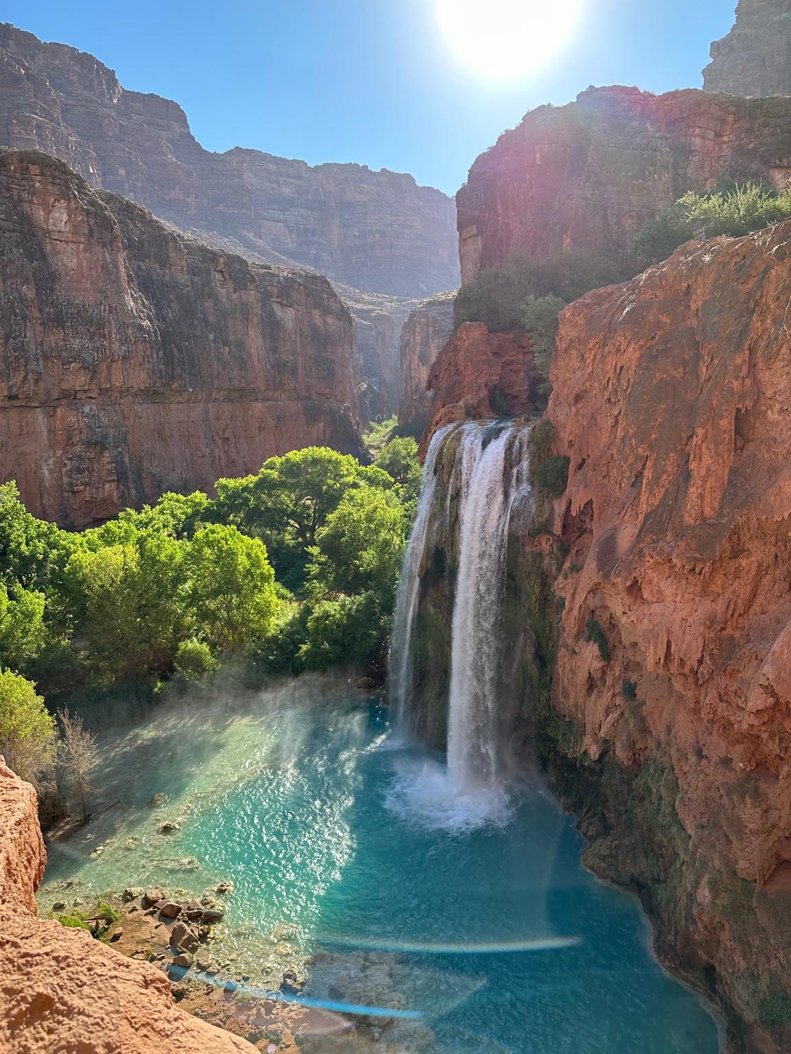 Scenic waterfall in Arizona surrounded by rocky cliffs and lush greenery under a bright blue sky.