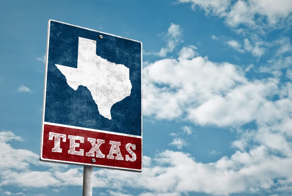 Vintage-style Texas road sign with a map outline against a blue sky with clouds.