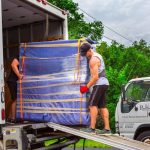 Professional movers carefully loading a wrapped piece of furniture onto a moving truck from Poseidon Moving & Storage.