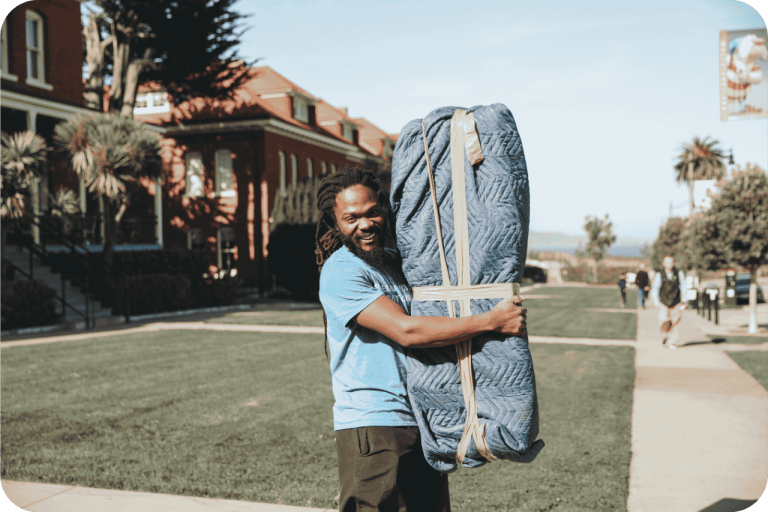 Poseidon Moving Company crew member smiling at the camera while holding a wrapped furniture piece in a moving blanket