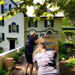 Professional movers from Poseidon Moving transporting wrapped furniture through a garden walkway.