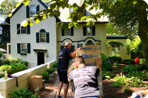 Professional movers from Poseidon Moving transporting wrapped furniture through a garden walkway.