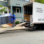 Poseidon Moving team loading a wrapped furniture piece onto a truck using a ramp.