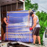 Poseidon movers loading a fully wrapped furniture item into a moving truck